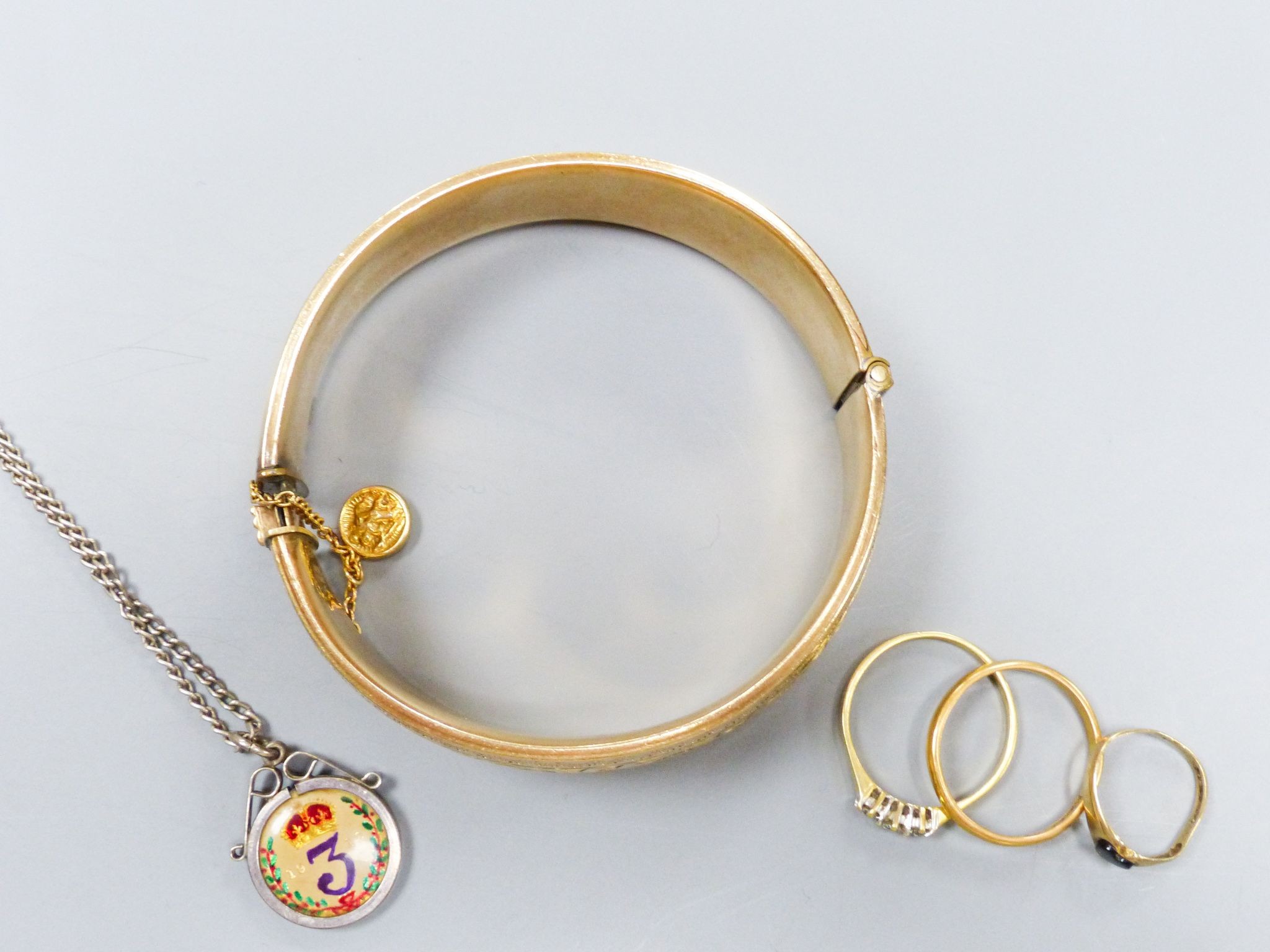 A filled 9ct gold (metal core) bangle together with a three-stone 18ct yellow gold diamond ring (gross 2.6g) a 22ct yellow gold wedding band (3.1g) and a further small gold ring and an enamelled coin pendant on chain (5)